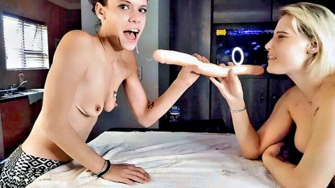 Two petite topless brunettes playfully sucking large white double dildo with small tits exposed