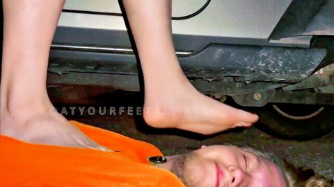 Barefoot woman tramples submissive man's face under her sole outdoors by car