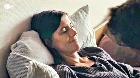 Brunette woman smiling relaxed in bed wearing sweater with man beside her
