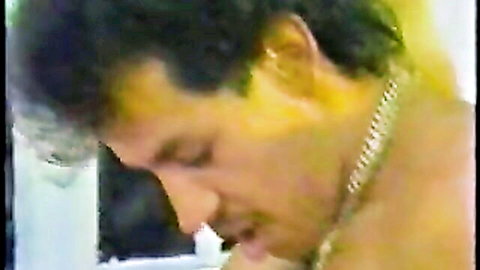 Closeup of curly-haired man with mustache and gold chain moaning in intense pleasure