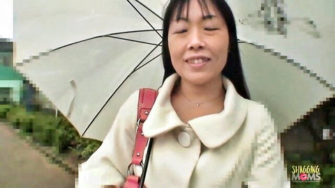 Smiling East Asian mature mom in white coat with red purse under umbrella