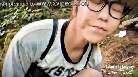 Cute Asian ladyboy smiles teasingly outdoors wearing glasses and gray tank top