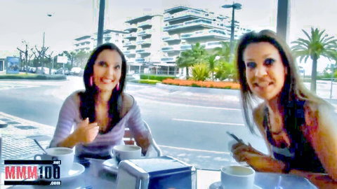 Two smiling brunette women in tank tops sipping coffee at outdoor cafe table