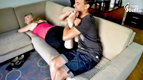 Blonde woman lying down as man worships her smelly bare soles in foot fetish scene