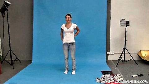 Slim brunette posing in white tee and jeans in studio, eager to strip naked