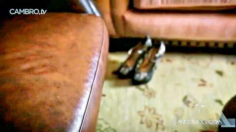 Sexy high heels kicked off beside brown leather couch on carpet