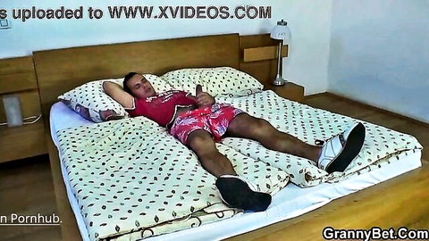 Man lying relaxed on bed in red floral shorts and white sneakers on GrannyBet