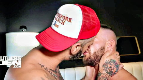 Tattooed muscular men passionately kissing, one in trucker hat