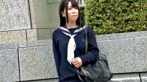 Cute Asian teen schoolgirl in tight navy sailor uniform standing outdoors with bag