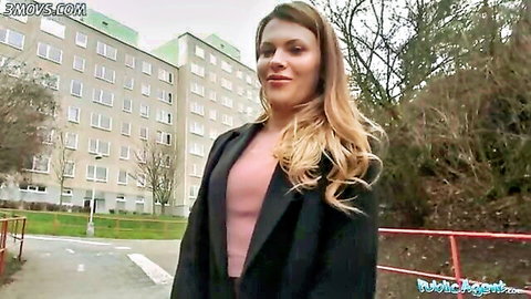 Blonde woman in black coat smiling seductively outdoors during public pickup