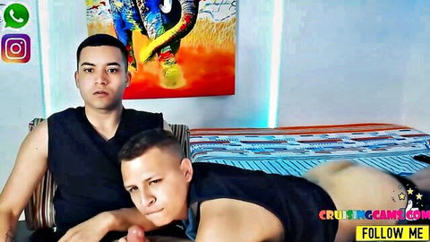 Two Latino guys in tank tops posing seductively, one hand on bulge
