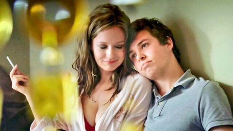 Blonde woman with deep cleavage cuddling handsome guy while smoking cigarette intimately