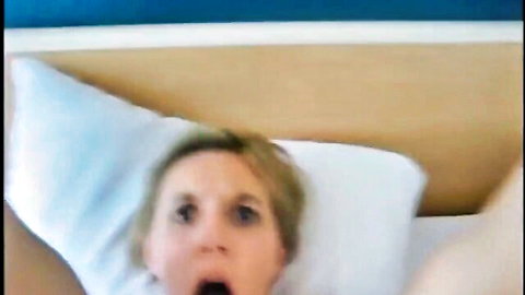 Shocked blonde woman with wide eyes and open mouth in surprise on bed amateur homemade