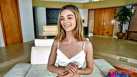 Petite blonde teen smiling happily in revealing white bralette showing small tits and underboob on couch