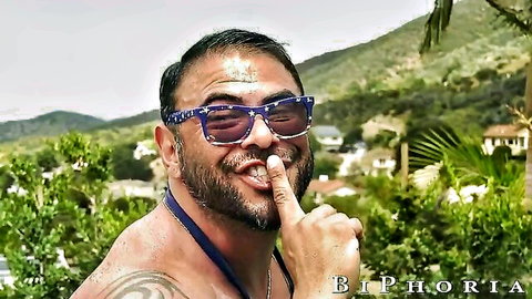 Shirtless muscular South Asian man with beard and tattoos by tropical pool, shushing gesture