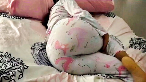 Curvy ebony woman in pink dinosaur pajamas teasing on bed