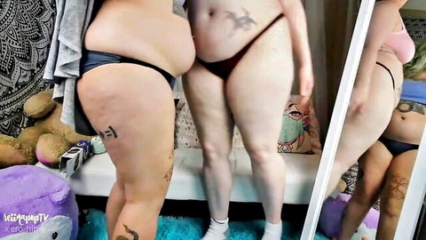 Curvy women in thongs posing mischievously in bedroom mirror