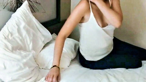 Busty white amateur babe teasing massive cleavage with crossed arms in tight white tank top on bed