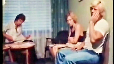 Blonde woman sits between two men in vintage room chatting clothed foreplay tease