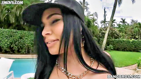 Sexy Latina brunette in backwards cap smiles teasingly by pool showing deep cleavage