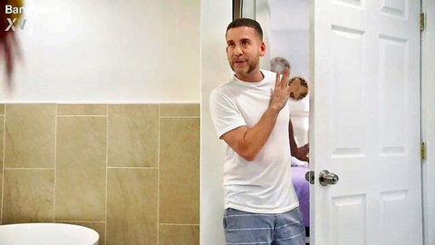 Handsome white guy in t-shirt and shorts holding foam in bathroom, roommate peeking at door