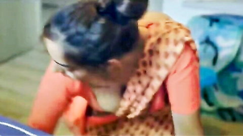 Desi mature woman in orange top and brown dupatta, sitting with cleavage tease