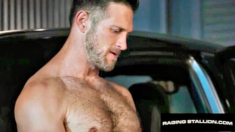 Hairy muscular man with gray beard leaning shirtless into black car door in garage