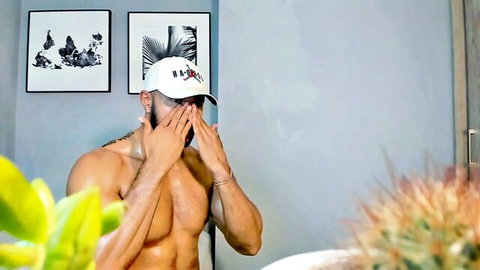 Muscular shirtless hunk in white cap covers eyes teasingly showing ripped abs