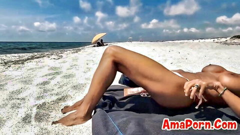 Topless tanned babe lounges on beach towel exposing bare tits and spreading legs in tiny bikini bottoms