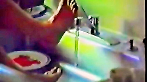 Bare foot with red toenails rinsing red plate under faucet in sink
