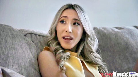 Busty blonde in low-cut yellow top sitting on couch with surprised open mouth