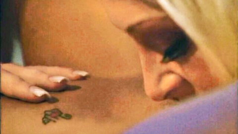 Blonde babe with pink nails seductively nuzzling muscular man's tattooed chest closeup