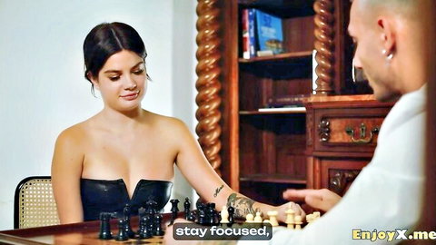 Sensual brunette babe with big tits in low-cut black dress plays chess teasing tattooed bald guy
