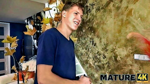 Handsome young brunette guy in blue shirt smiling in kitchen holding tablet for mature taboo sex