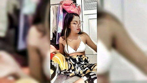 Young Latina teen in white lace bralette showing cleavage, sitting legs spread in colorful pants in closet