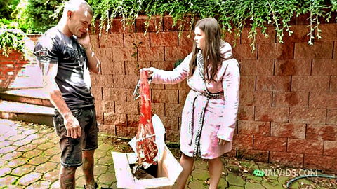 Taylee Wood in pink bathrobe holding red cloth with tattooed man in outdoor gangbang teaser