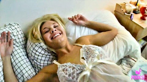 Blonde Remi in lacy white lingerie, smiling relaxed on bed