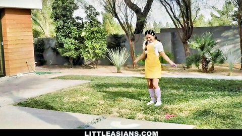 Cute petite Asian in yellow dress, pigtails and thigh-high socks posing playfully outdoors