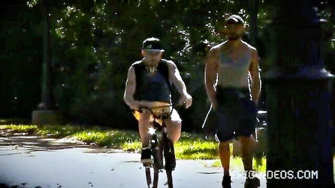 Two athletic men biking and walking outdoors in shorts and tanks
