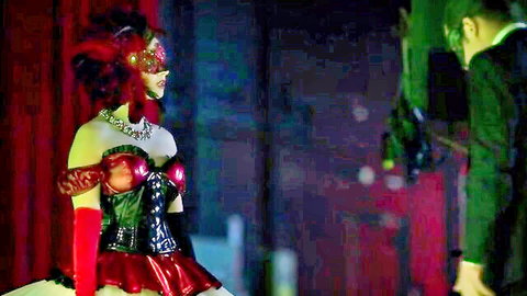 Annabel Barrett in red feathered corset and mask, seductive pose with man in suit from This Game's Called Murder (2021)