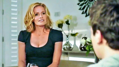 Blonde woman in low-cut black dress showing deep cleavage holds wine glass smirking at young man