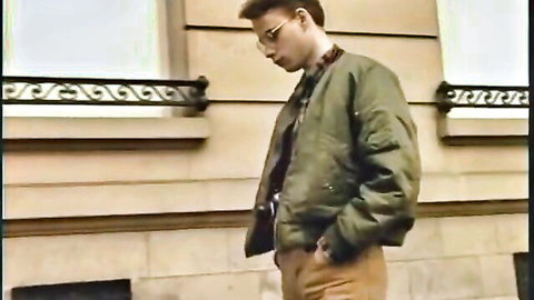 Vintage retro man in green bomber jacket standing outdoors against beige stone building