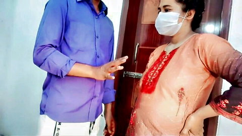 South Asian couple in masks flirt naughtily at wooden door fully clothed