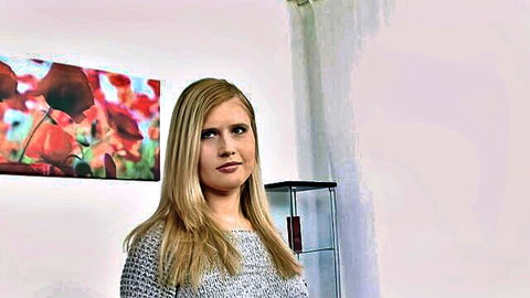 Blonde woman in gray sweater standing indoors with pursed lips ready for intense fuck