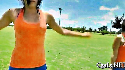 Two fit Asian women in orange tank tops and shorts outdoors on field
