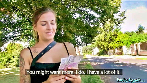 Blonde babe with tattoos holds thick stack of cash between her cleavage smiling outdoors