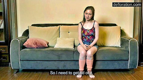 Petite brunette teen in tiny shorts and colorful tank top sitting on couch with socks