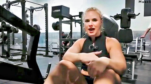 Blonde athletic woman in gym tour on rowing machine, smiling