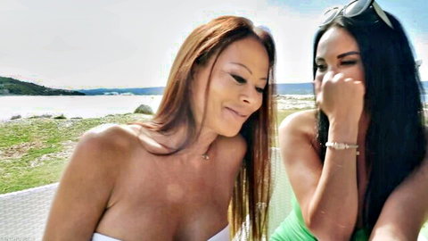 Two busty brunette Latinas with huge tits cleavage smiling flirtatiously by the lake