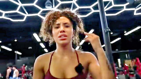 Curly-haired mixed woman in red tank top during intense gym leg day vlog